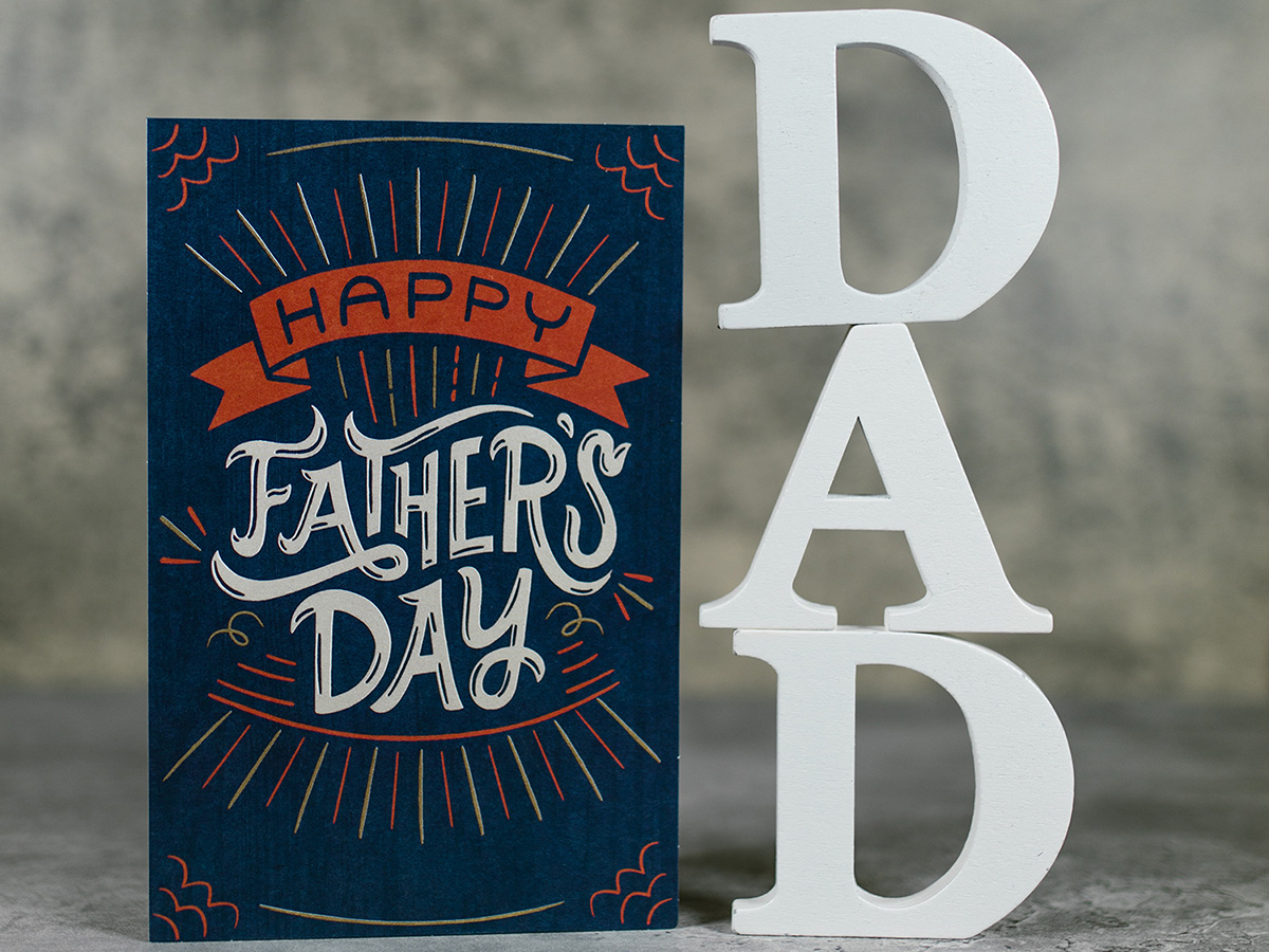 Image of a fathers day card with wooden letters reading DAD cut out next to it.