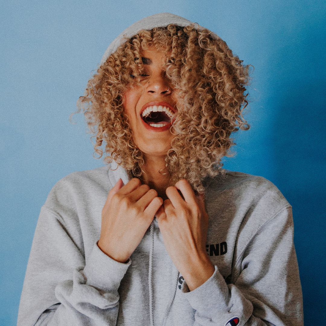 happy young adult woman smiling at camera while standing in-front of a blue wall
