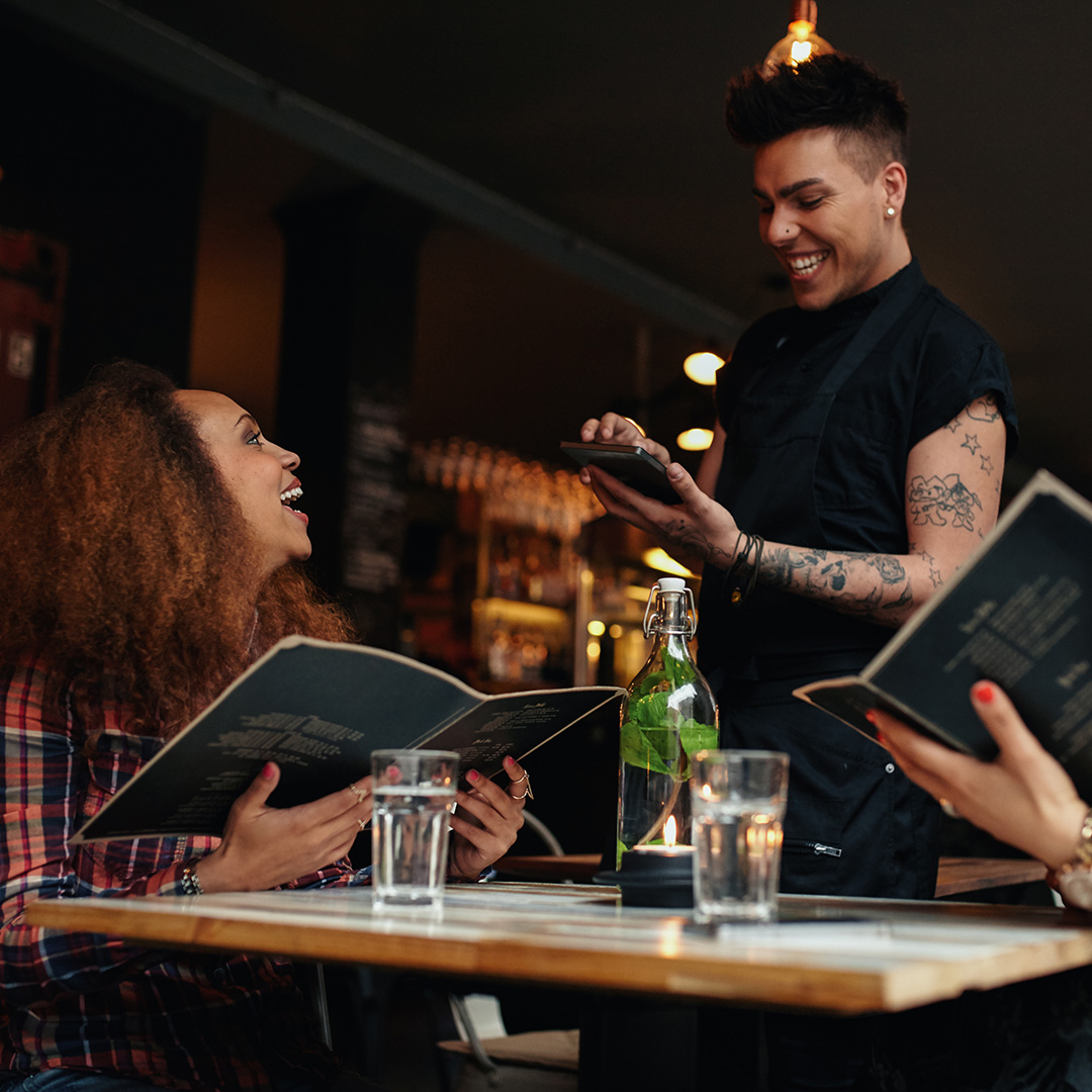 A waiter laughing with a customer while taking their order