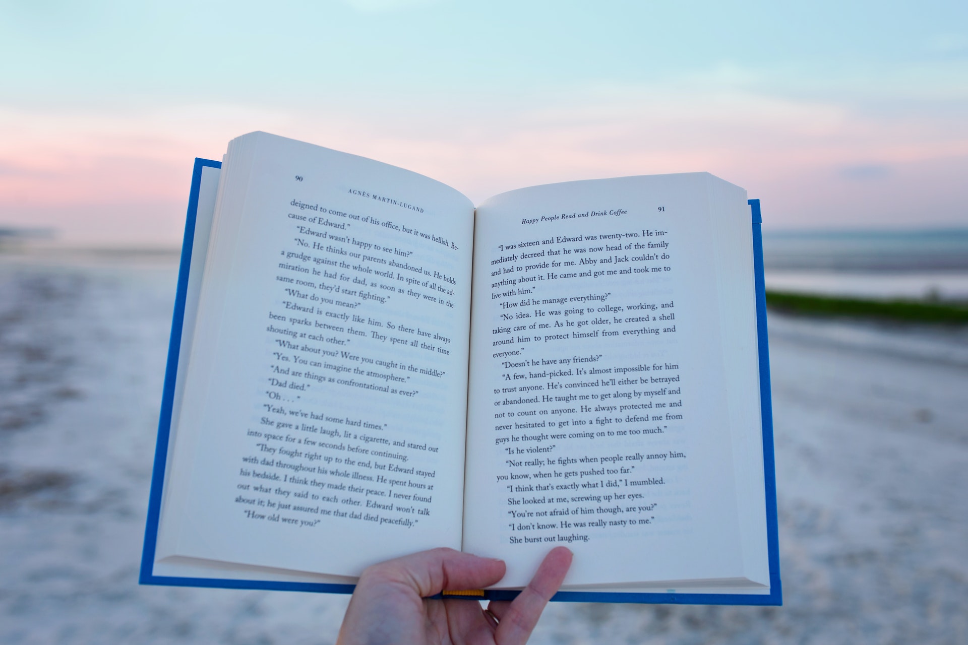 Opened spread of book pages in front of sunset on the beach.