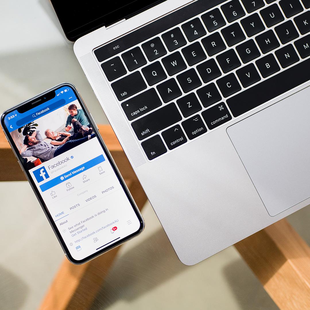 A close-up of a phone with facebook on it next to a computer keyboard