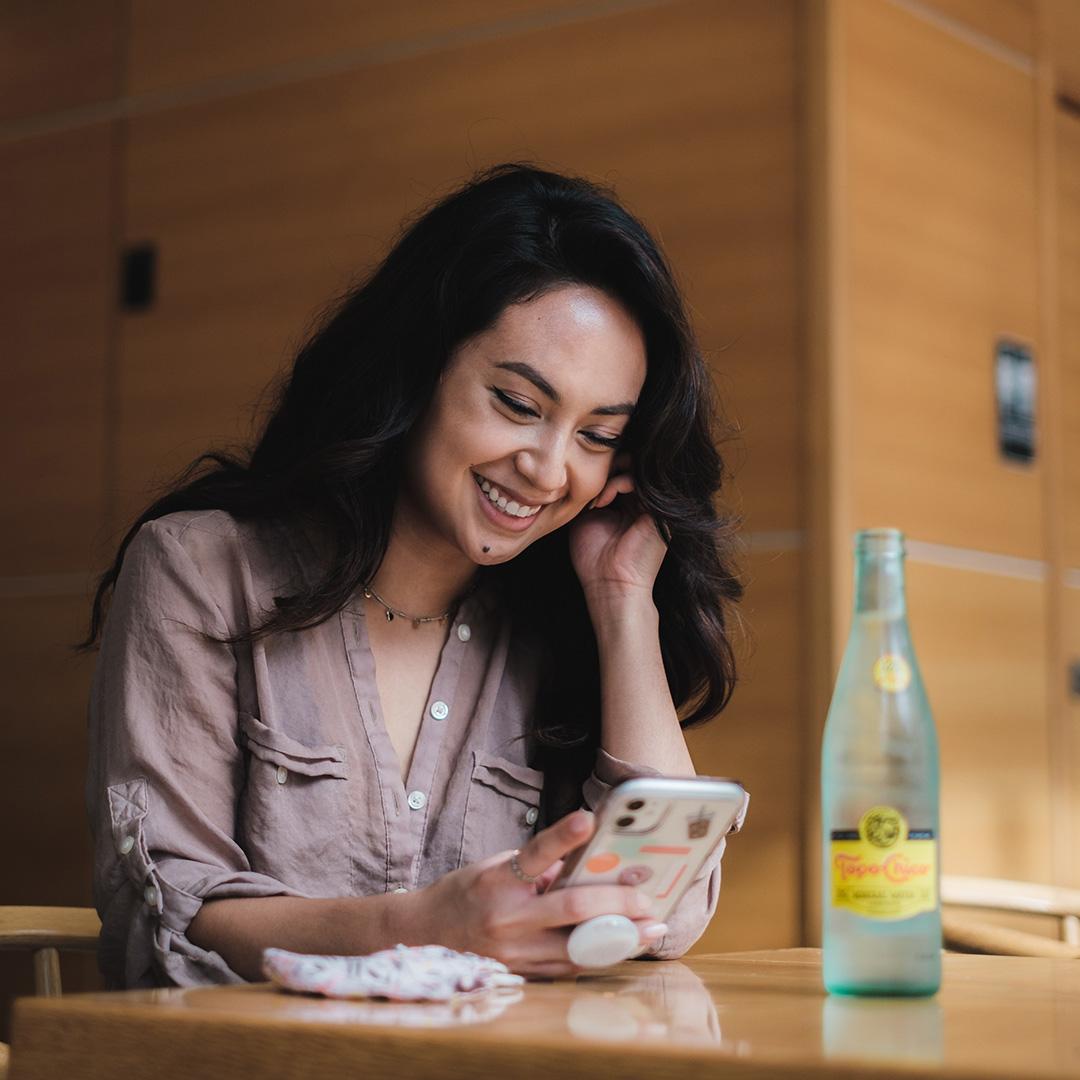 A woman at a restaurant looking happily at her phone