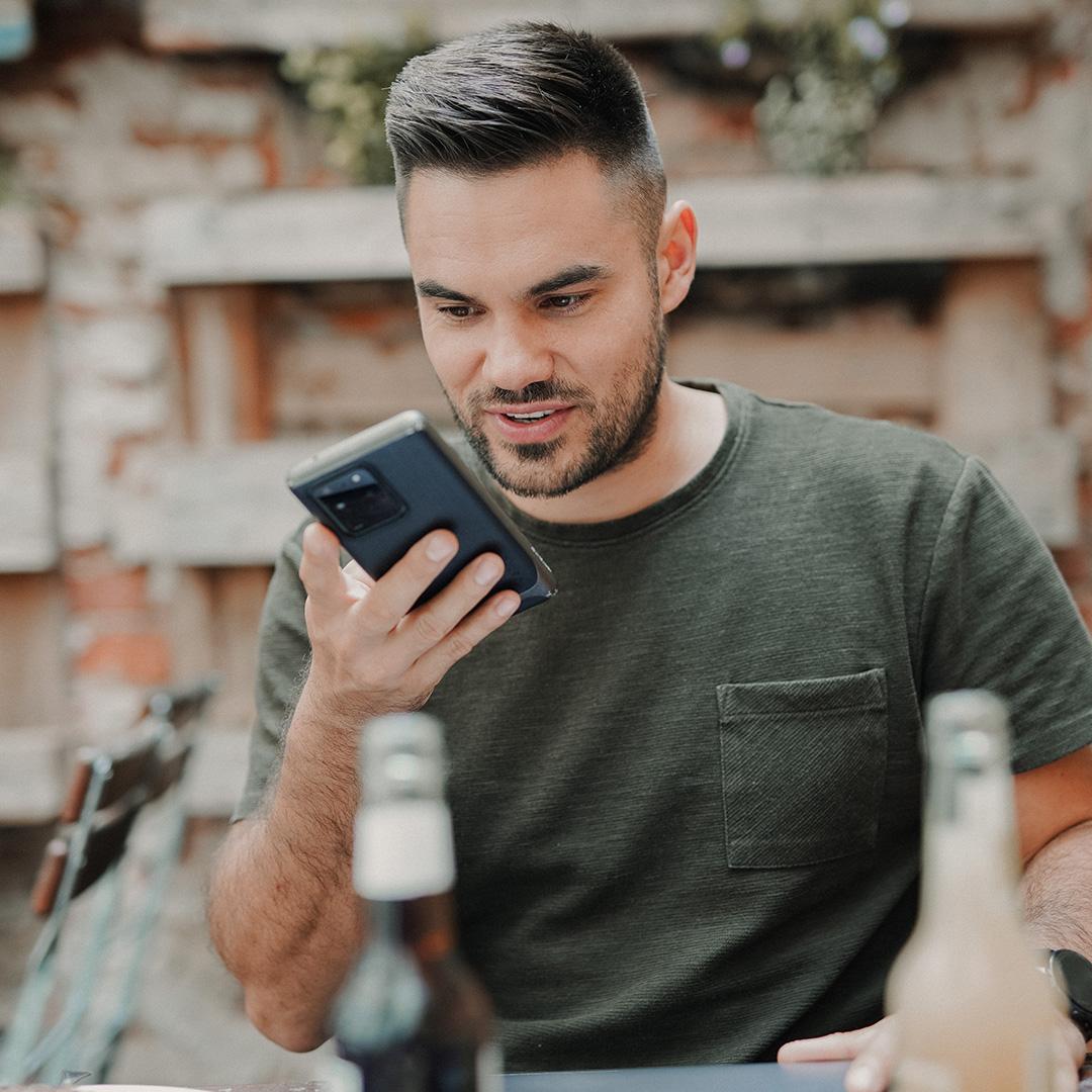 A man sitting at a cafe using voice commands to search on his phone