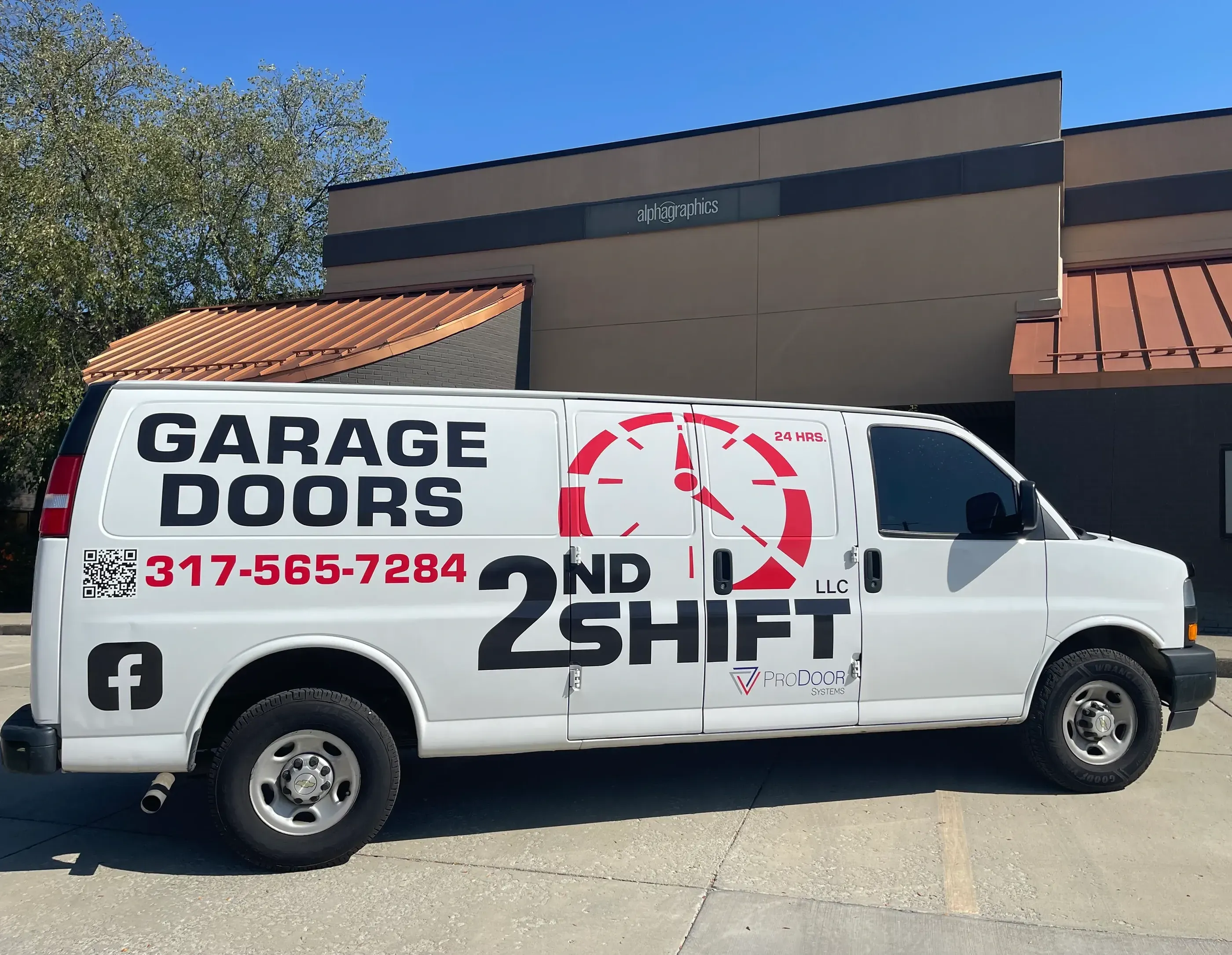A white van with bold red and black lettering advertising 2nd Shift Garage Doors. The design features the company name, logo with a clock graphic, a phone number, and a QR code on the side.