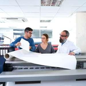 Three people at a print shop looking at a large format print