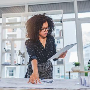 A businesswoman comparing a blueprint to an image on her tablet