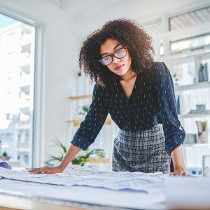 Young businesswoman looking at blueprints in her office
