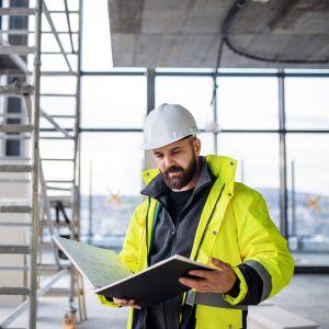 An engineer on a job site looking at a blueprint booklet