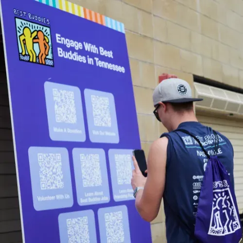 A man scans a QR code with his phone from a poster full of QR codes linking to information