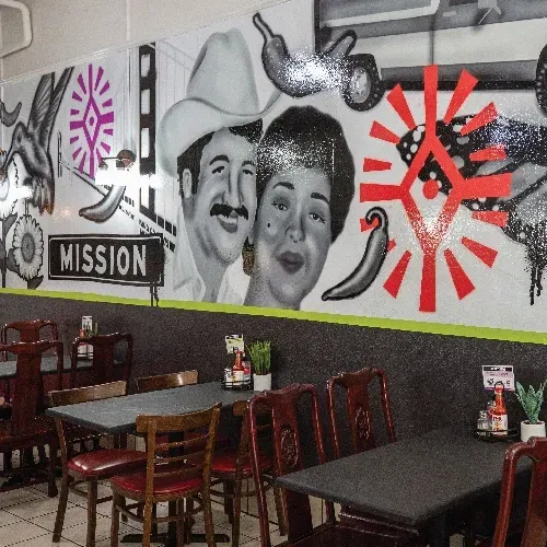 Restaurant wall with mural of black-and-white portraits, peppers, street signs and colorful design elements