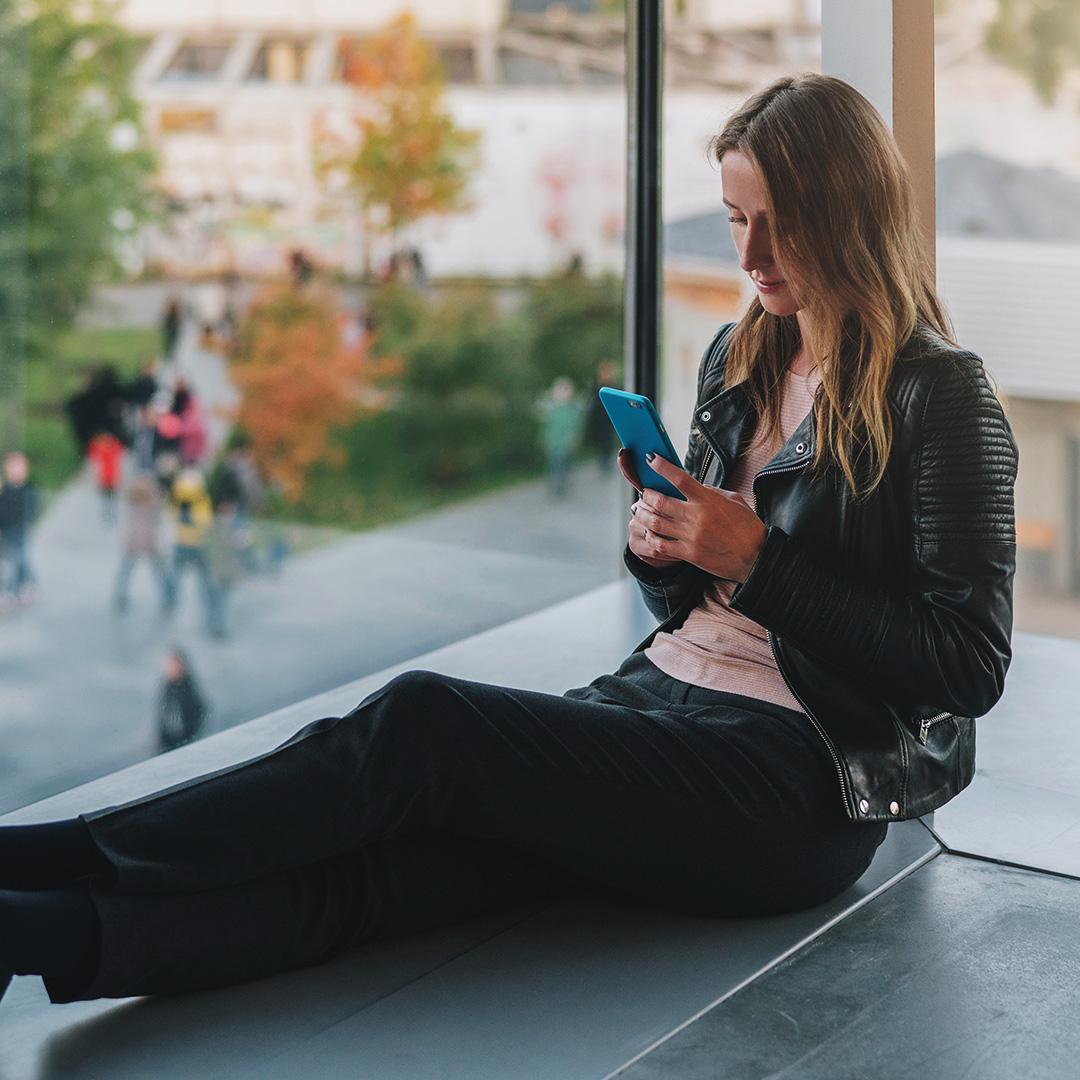 woman sitting on ledge typing on her phone