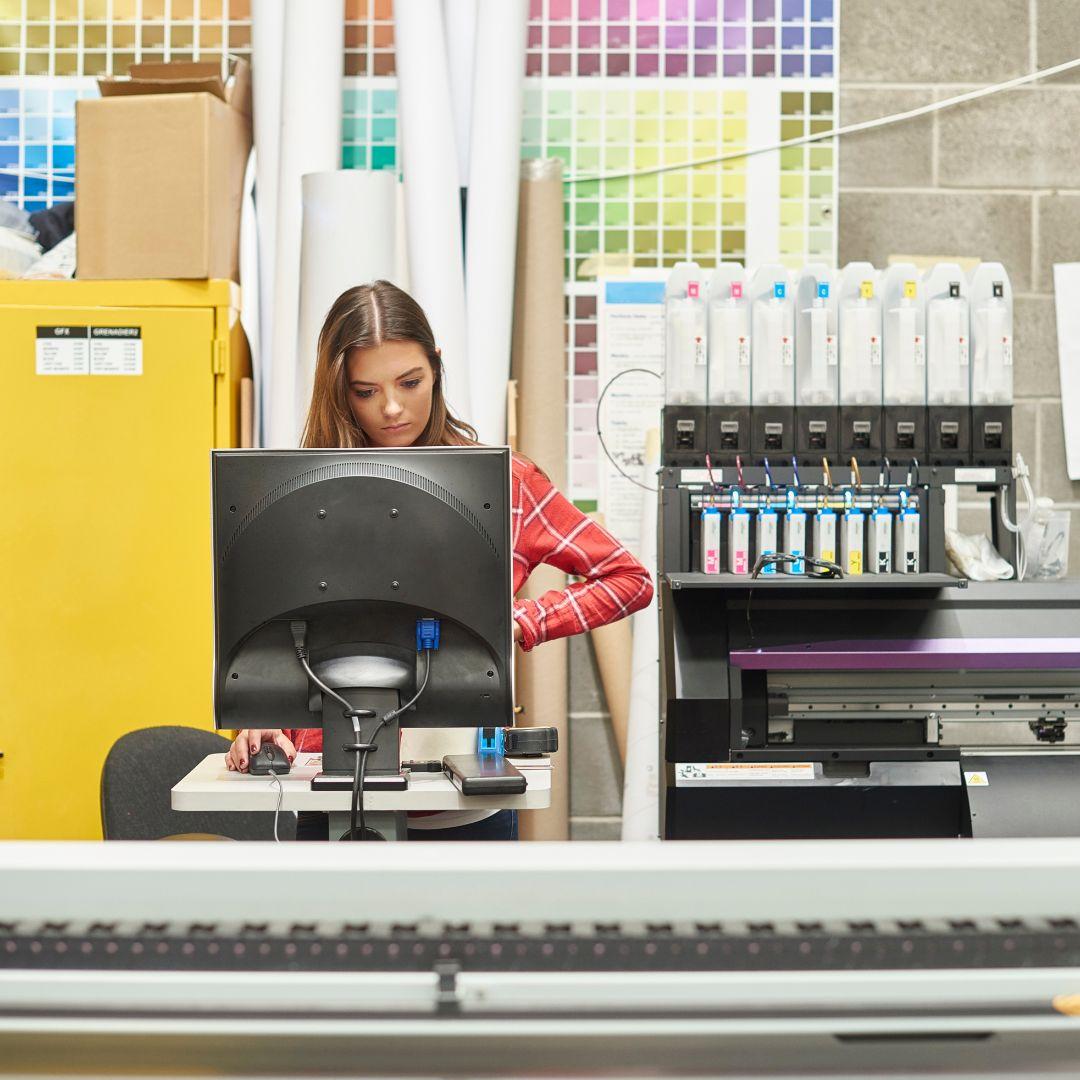 A printing professional working at a computer and large format printer