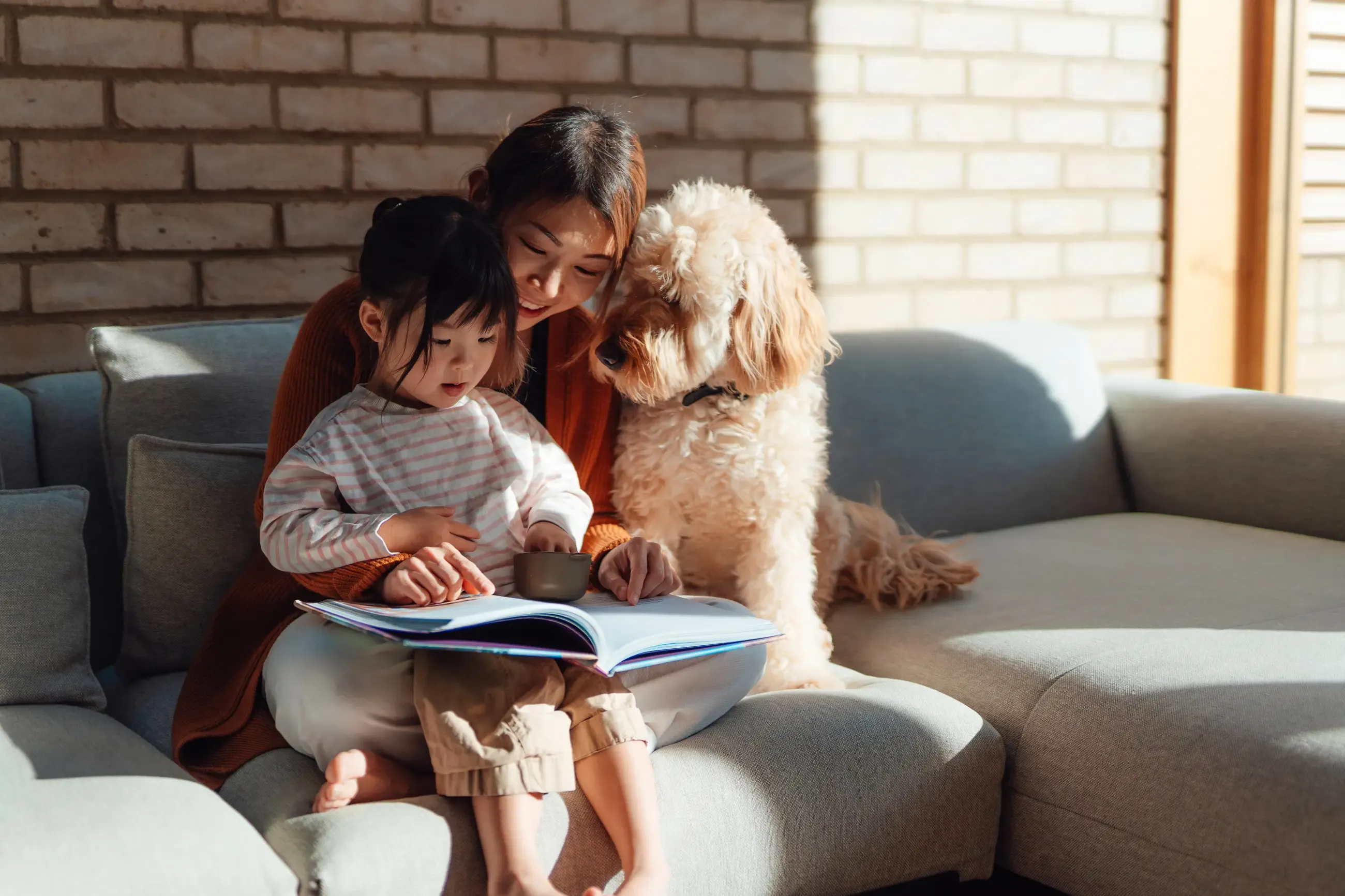 A woman and child with a dog sitting on a couch and reading a book