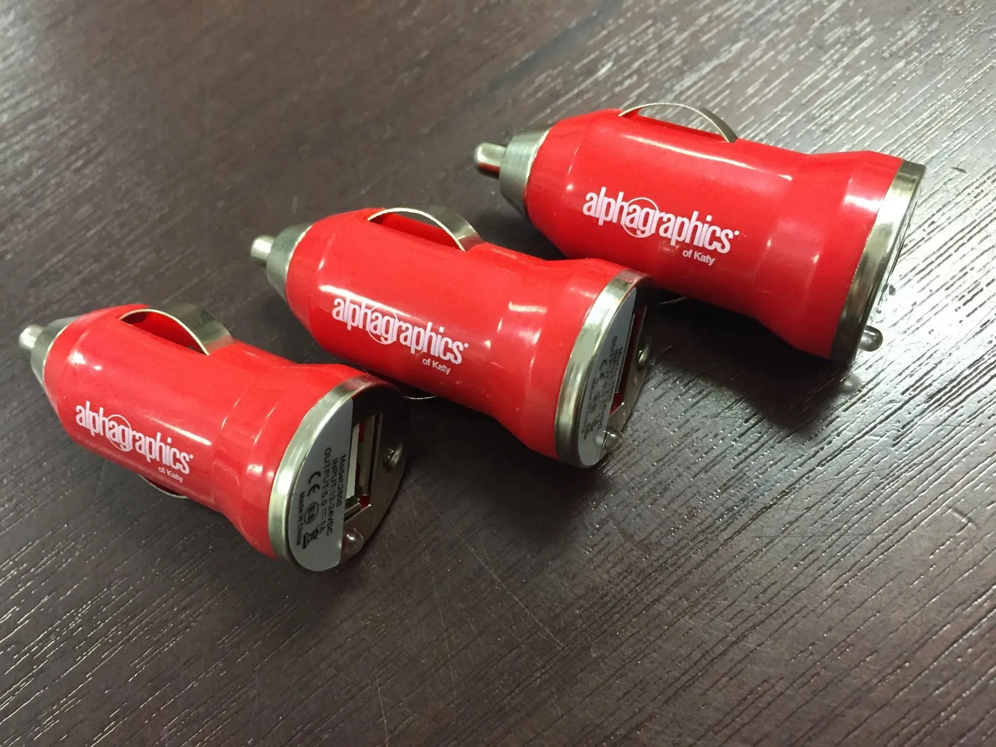 Red USB car chargers printed with the AlphaGraphics logo