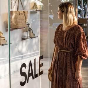 A woman looking at a store window with a sale sign