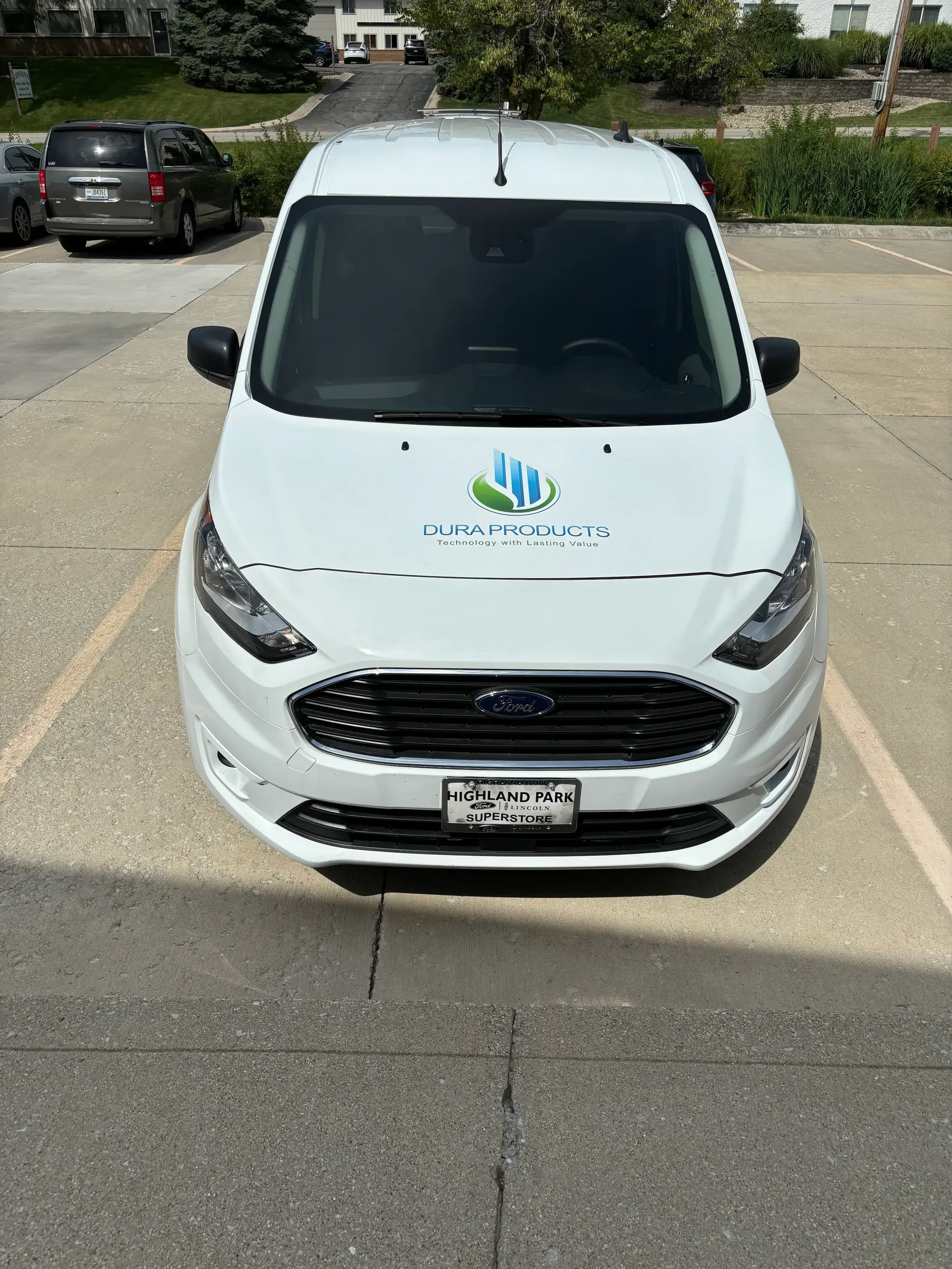 A white van viewed from the front, featuring the Dura Products logo and tagline “Technology with Lasting Value” prominently displayed on the hood.