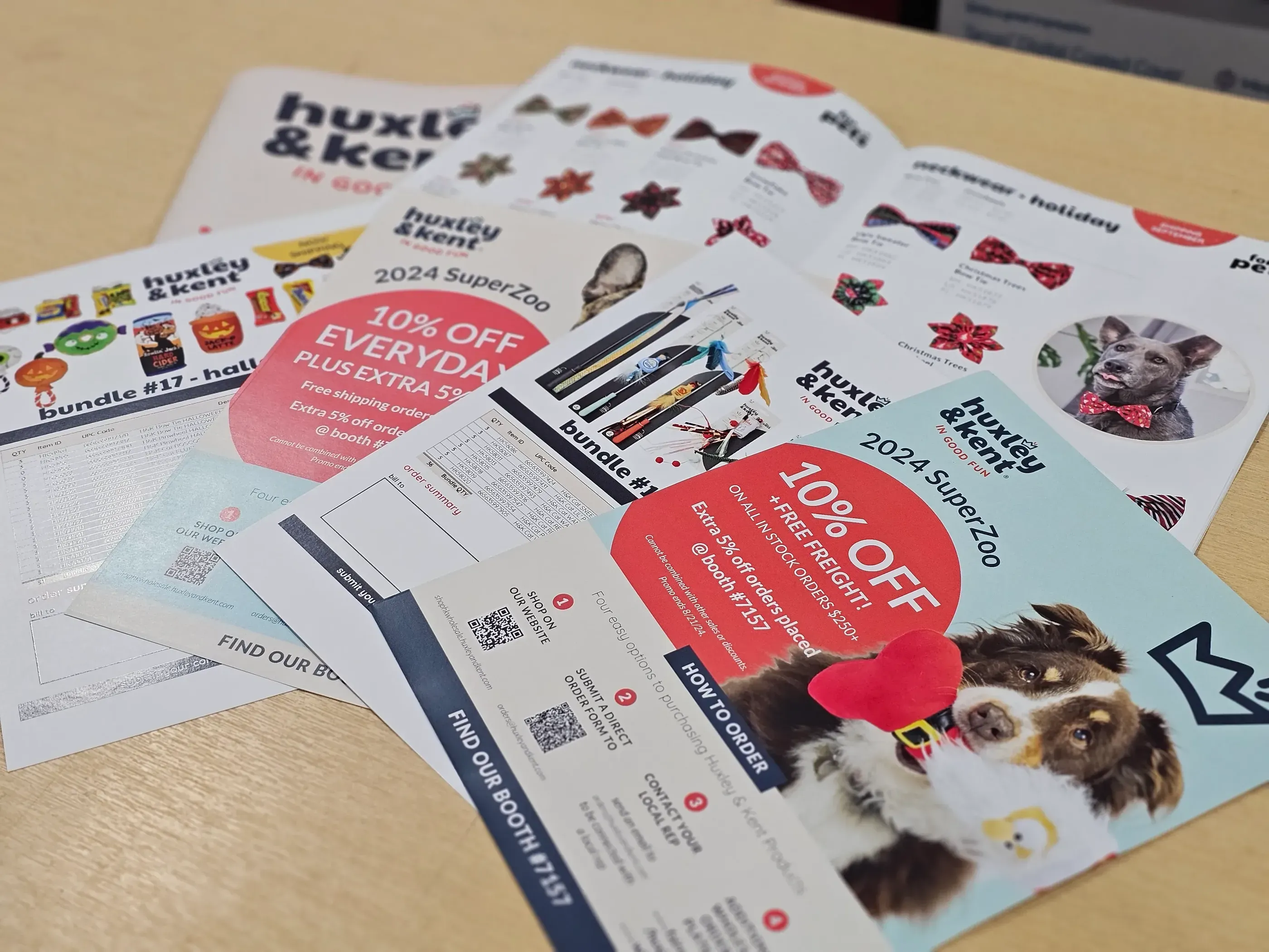 Assorted promotional materials for Huxley & Kent at SuperZoo 2024, including colorful product catalogs, discount flyers, and event brochures showcasing pet products and special offers.