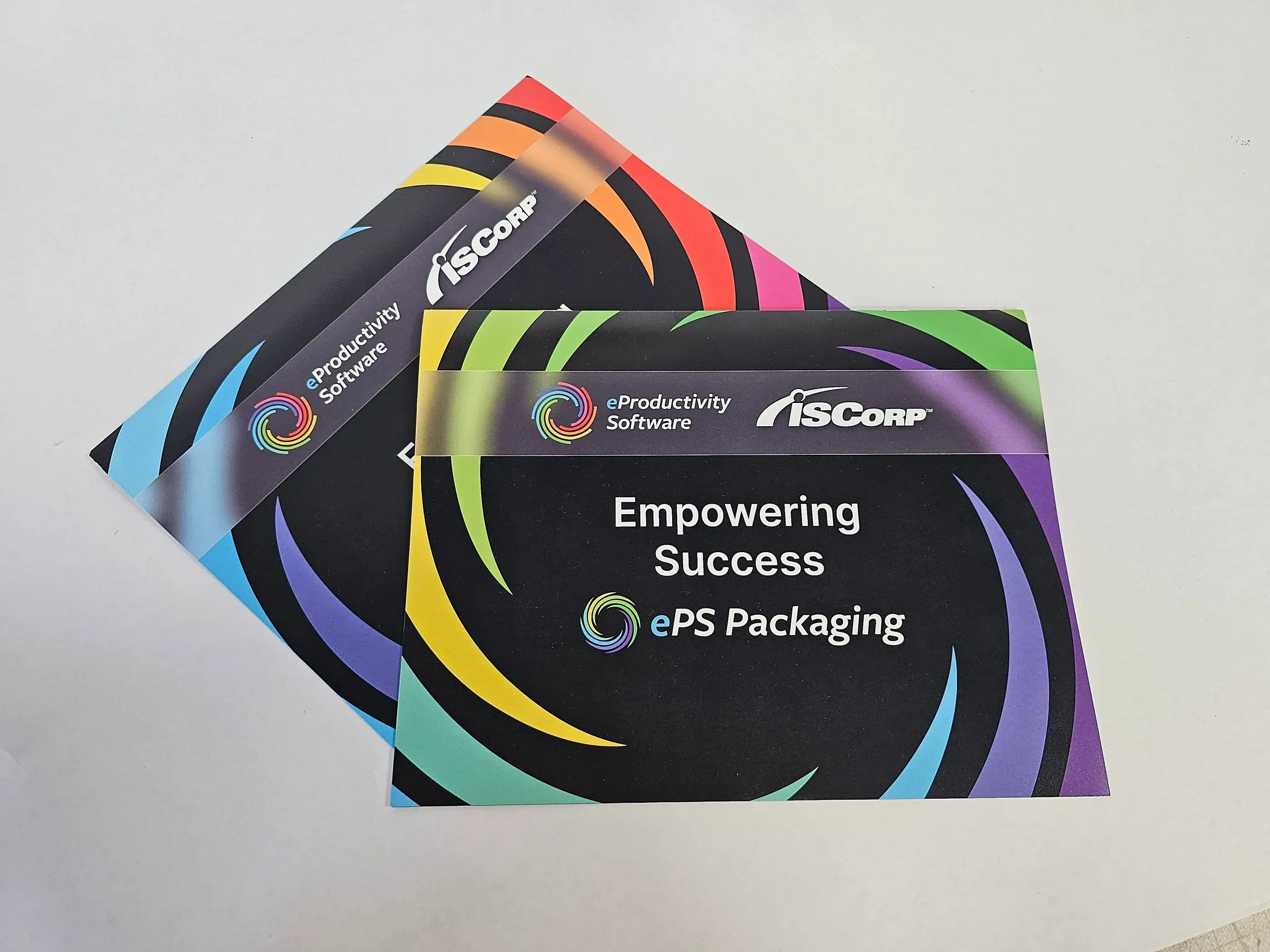 Two ISCorp multi-page booklets titled ‘Empowering Success: ePS Packaging,’ featuring colorful swirling designs and branding for eProductivity Software, used for promotional purposes at an event