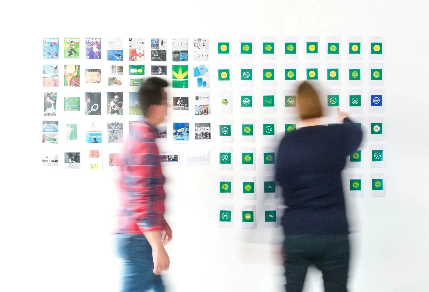 Two people looking at various cards on a wall of various versions of a company's brand identity.