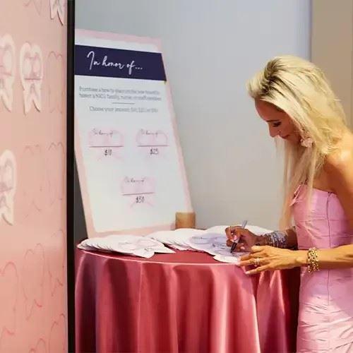 Woman writing on a paper bow next to a wall displaying other bows with written donation pledges