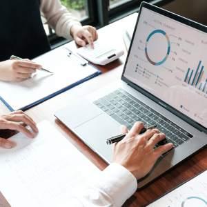 Two people at a desk looking at finance graphs on a laptop