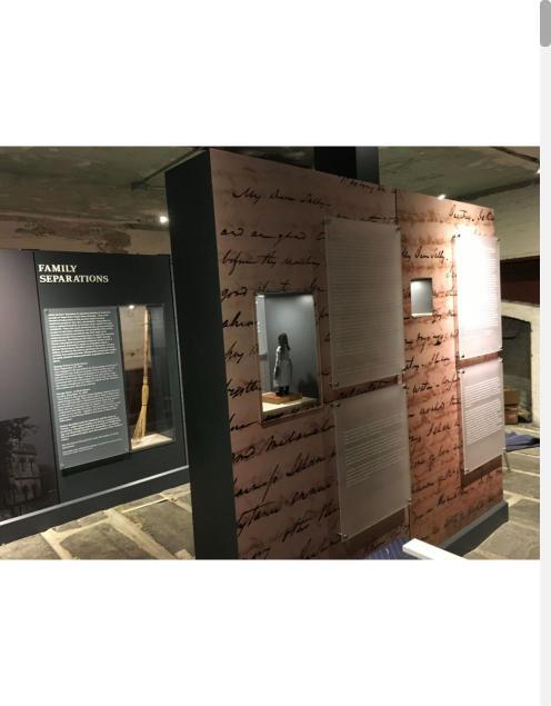 Museum exhibit wall with handwritten-script graphics and display cases