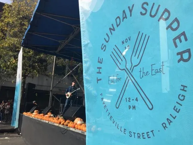 The Sunday Supper event banner beside a stage in downtown Raleigh
