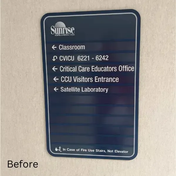 Before image of a directional sign at Sunrise Hospital. The sign lists key areas like the CVICU, Critical Care Educators Office, and Satellite Laboratory, with arrows directing to each. The older design features a plain blue background with white text.