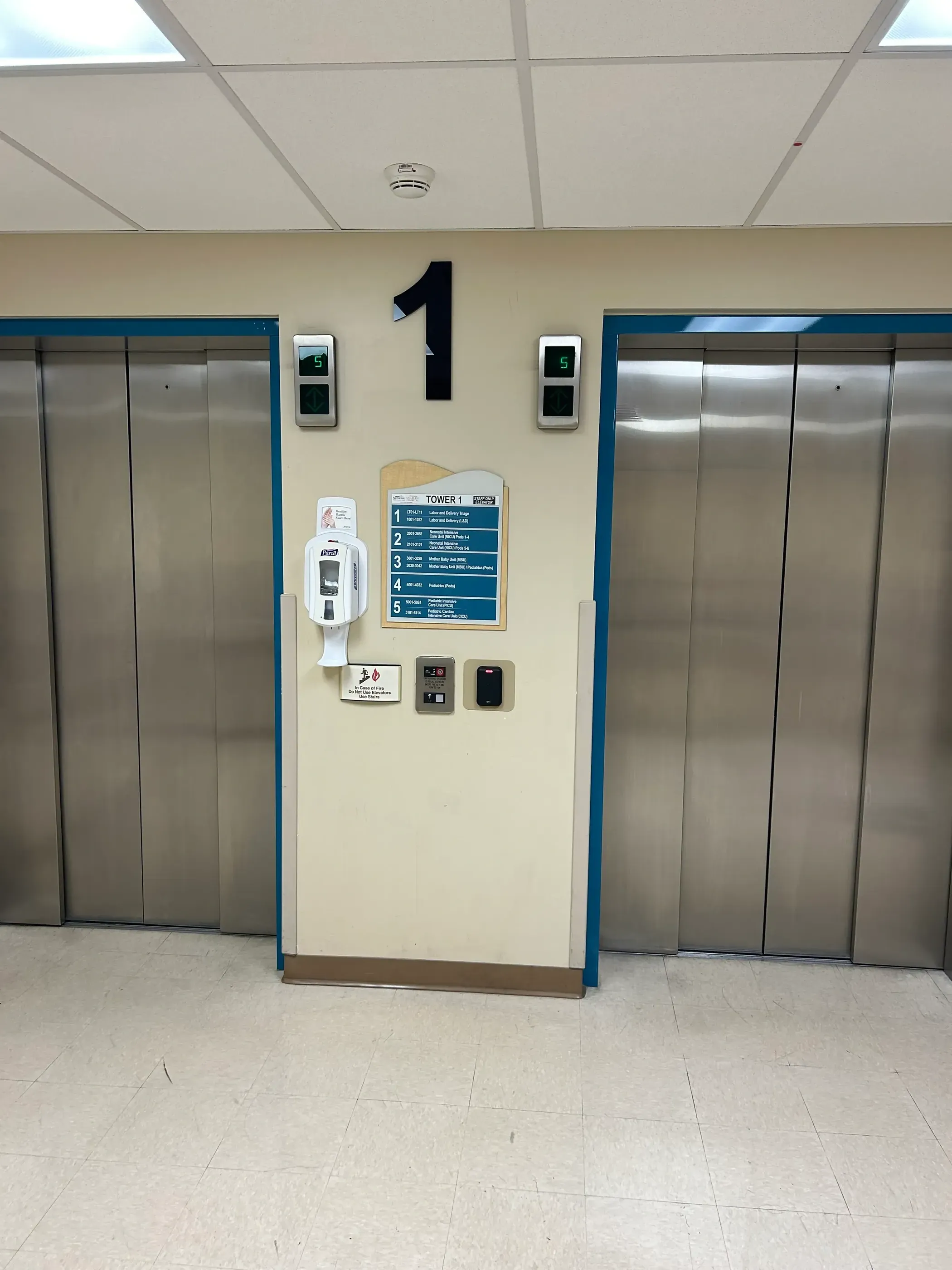 Tower 1 elevators at Sunrise Hospital featuring updated wayfinding signage. The number ‘1’ is prominently displayed above the elevators, with a floor directory and hand sanitizer station placed between them for visitor convenience.