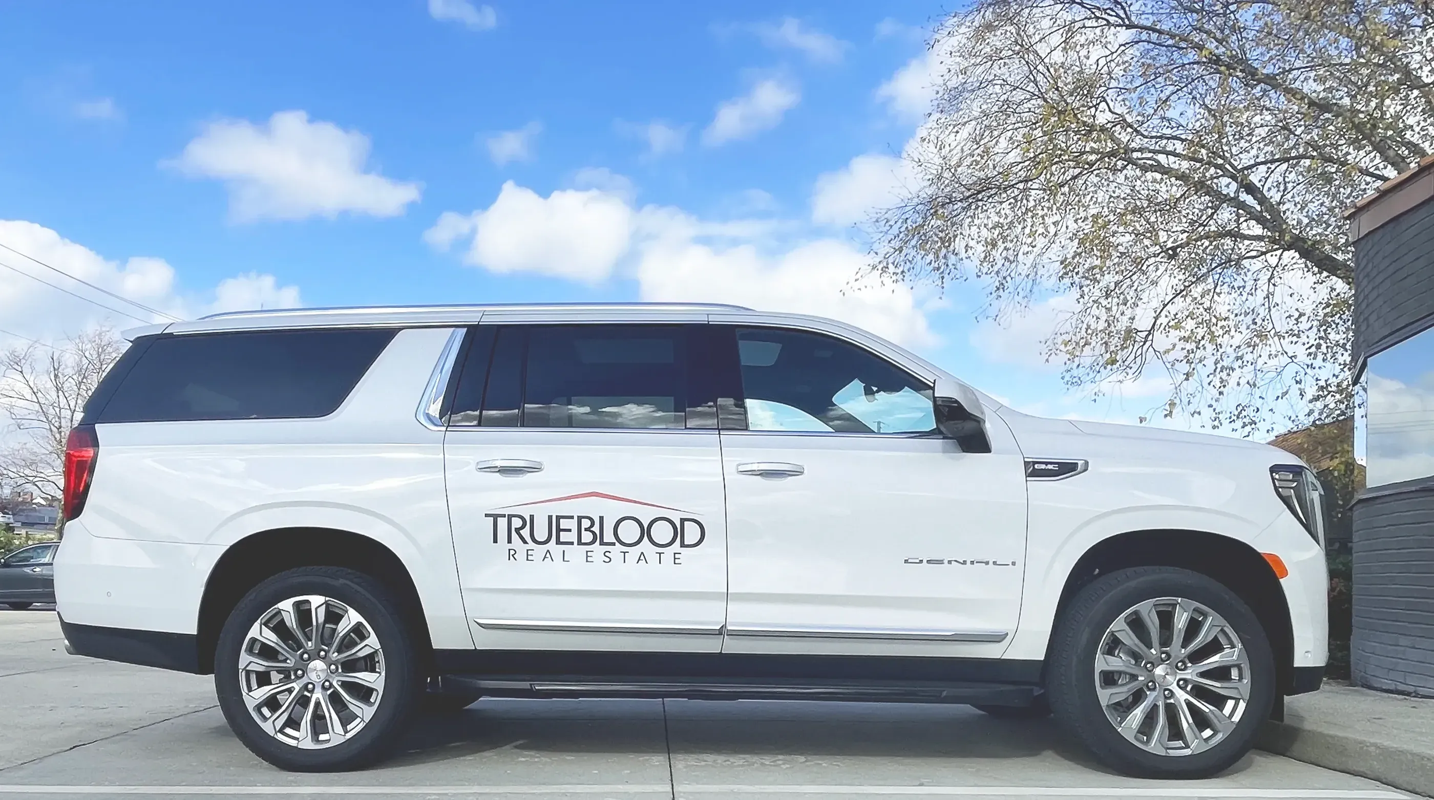 A sleek white SUV with a minimalist decal for TrueBlood Real Estate, featuring a clean logo with a red accent roofline design, emphasizing professionalism and brand clarity.